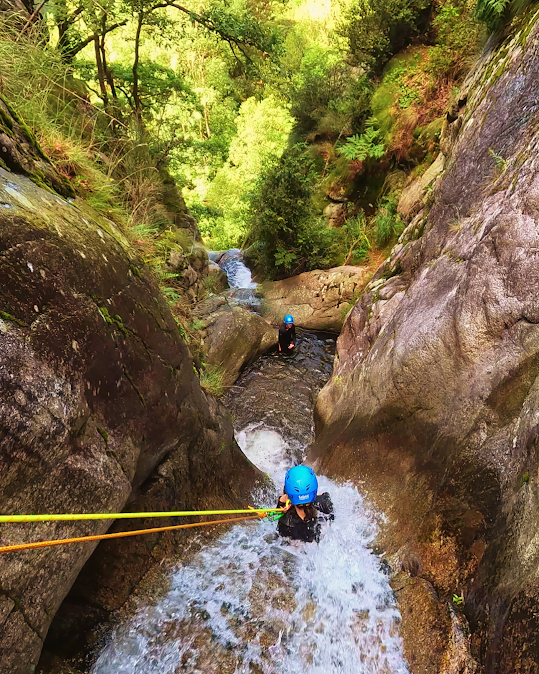 Personas descendiendo en rapel por una cascada en un estrecho cañón. El agua corre entre las rocas, con árboles al fondo.