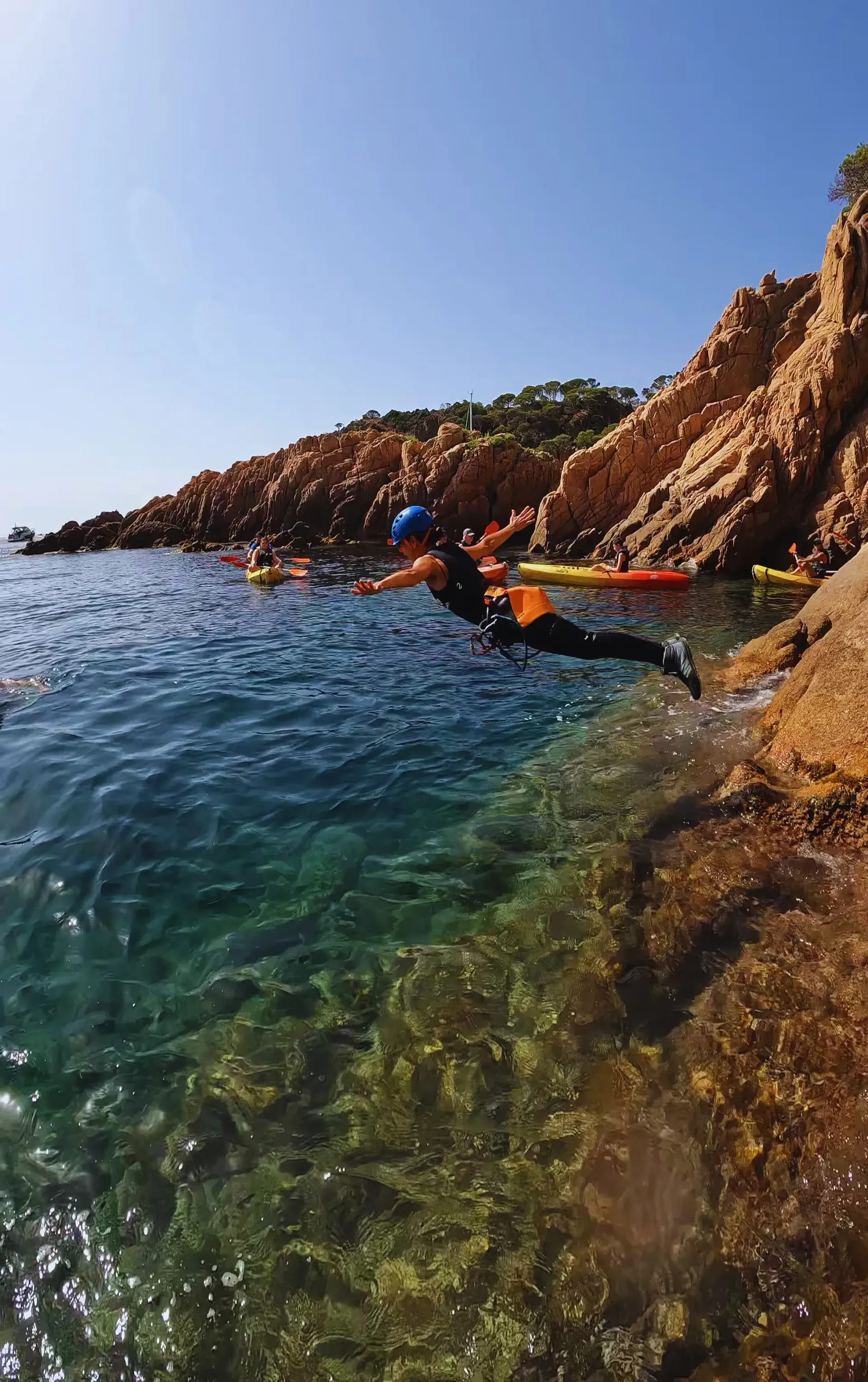 Una persona se sumerge en el océano desde una orilla rocosa.
