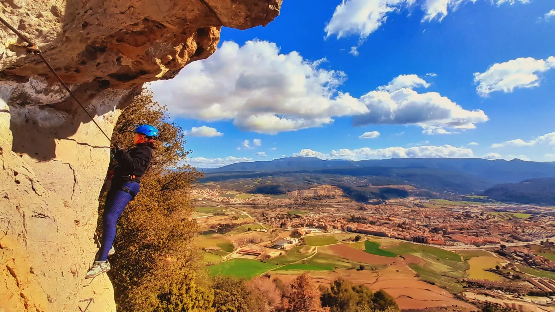 Una persona está escalando una pared de roca con vistas a una ciudad.