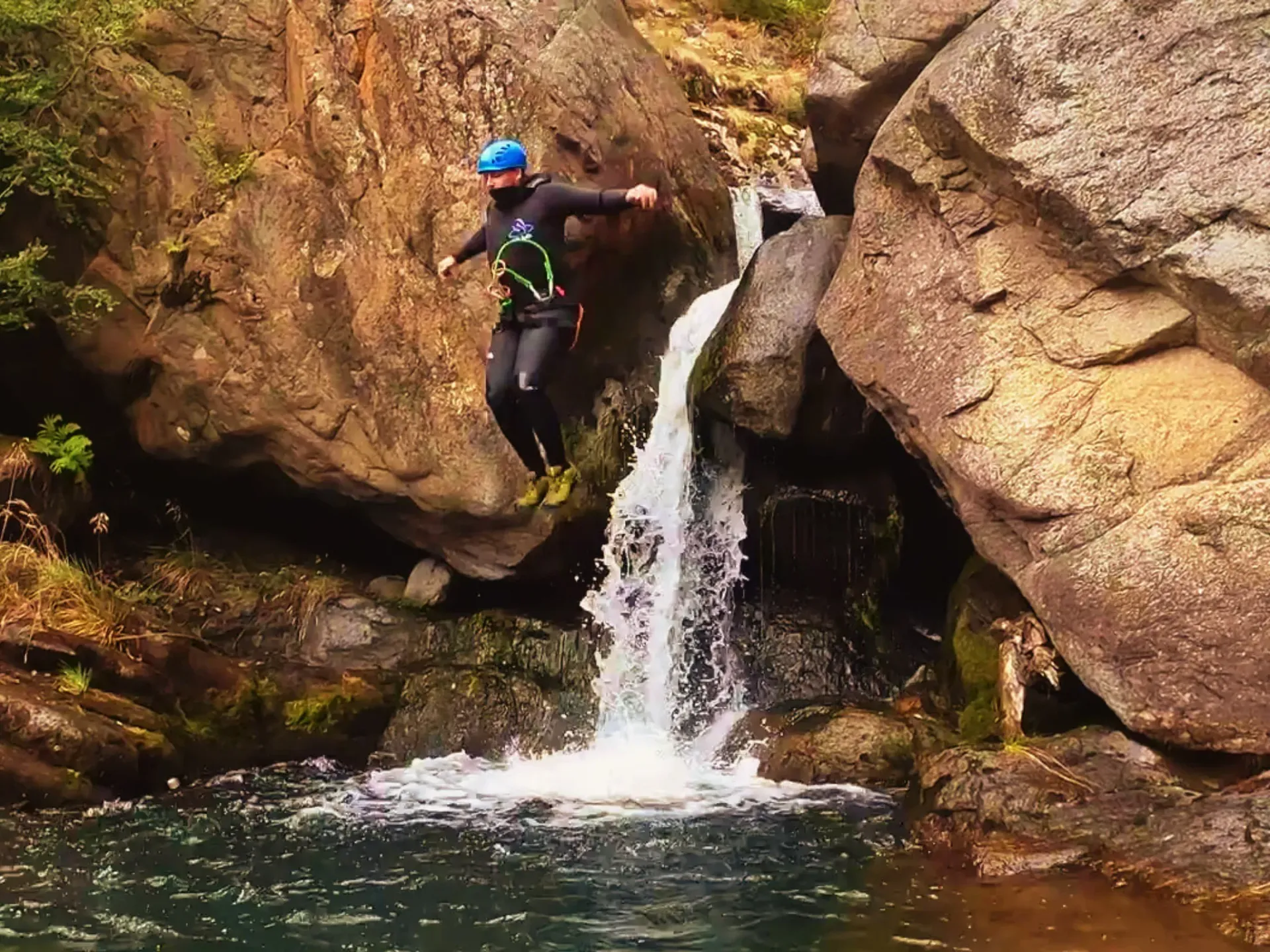 Un hombre salta desde una roca hacia una cascada.