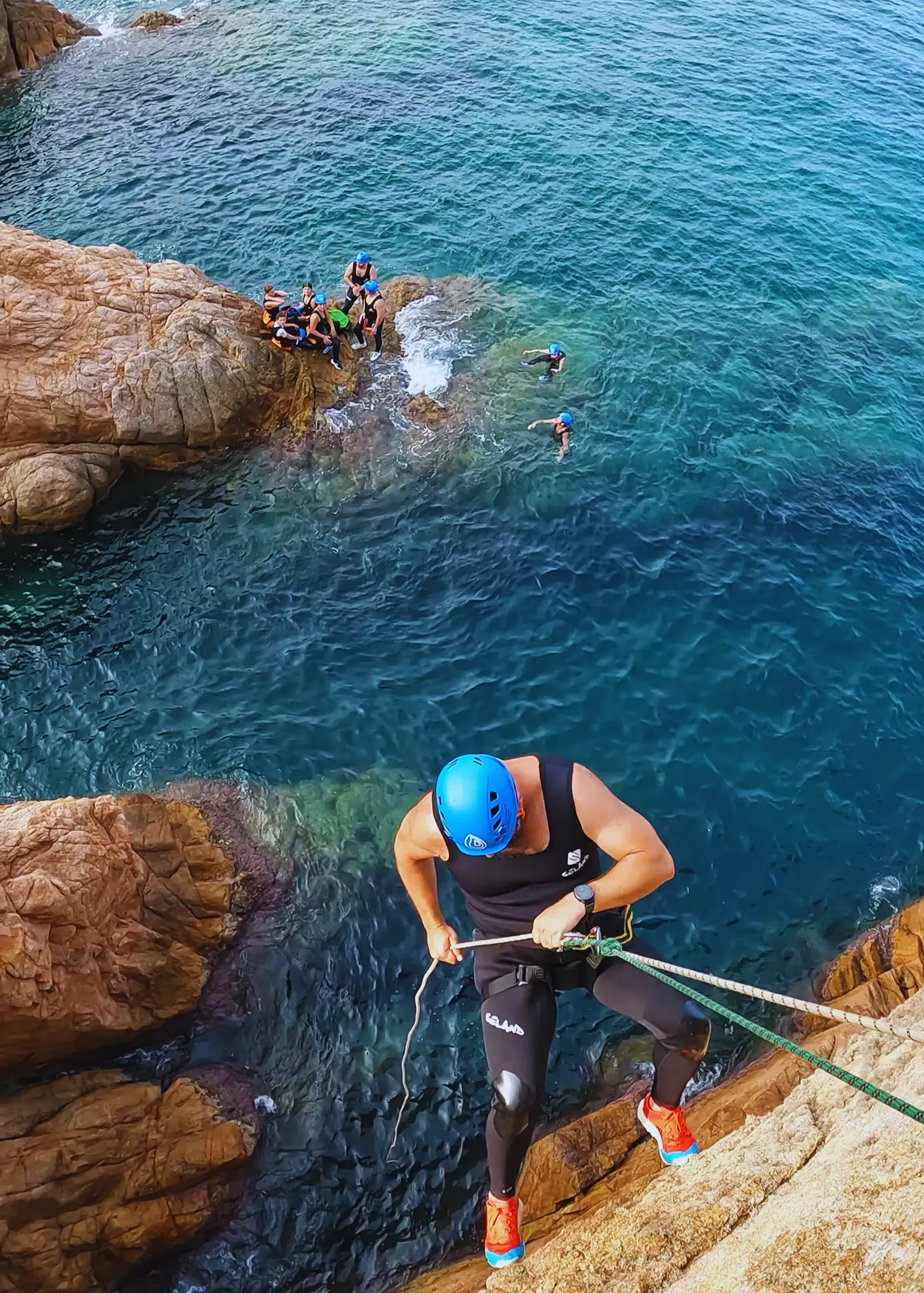 Un hombre está escalando un acantilado hacia el océano.