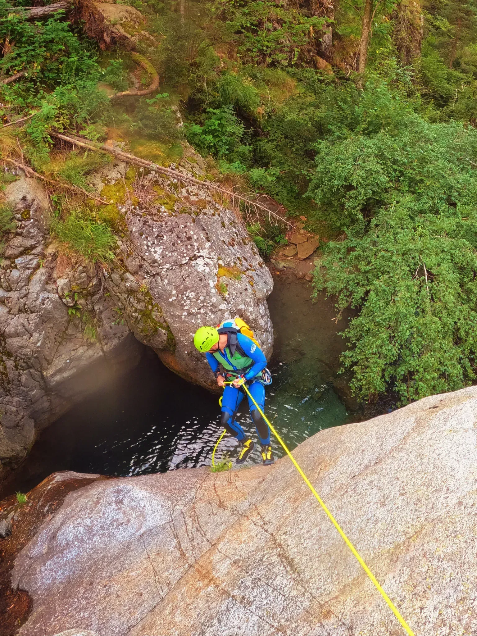 Una persona está bajando por una cuerda por un acantilado rocoso hacia un río.