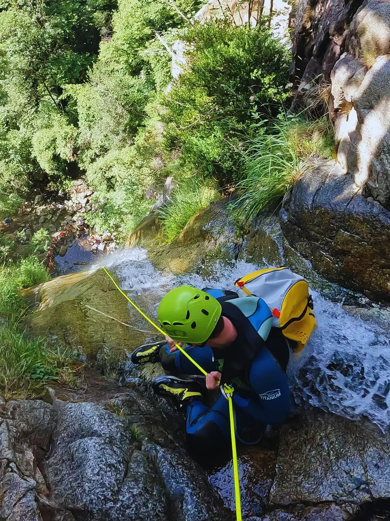 Una persona que lleva un casco está arrodillada sobre una roca al lado de una cascada.