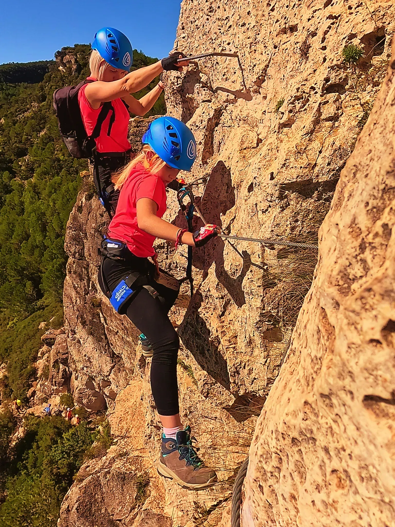 Dos jovencitas están escalando un acantilado rocoso.