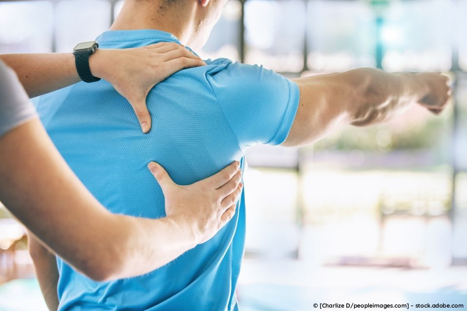 Ein Therapeut in einer Physiotherapiepraxis untersucht den oberen Rücken und die Schulter einer Person
