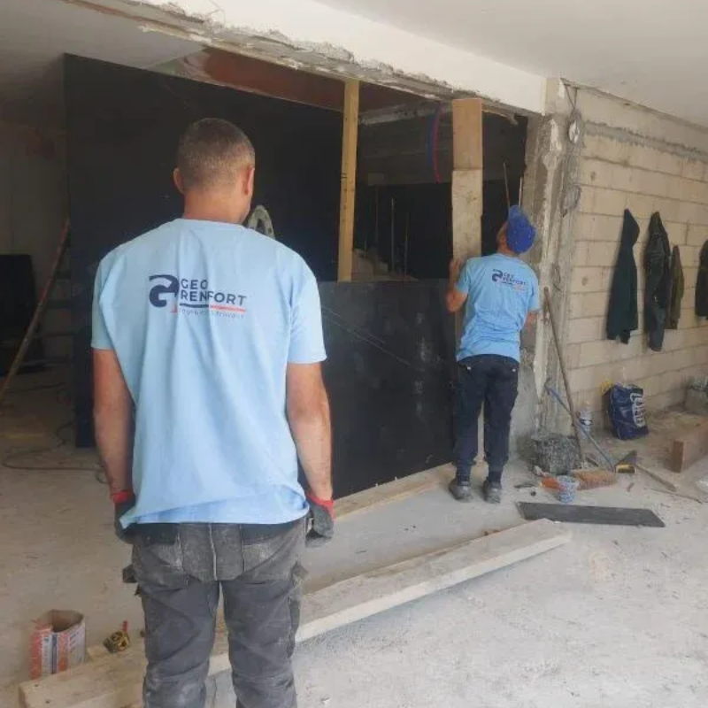 Deux ouvriers installent un panneau sombre à l'intérieur d'un bâtiment en construction.