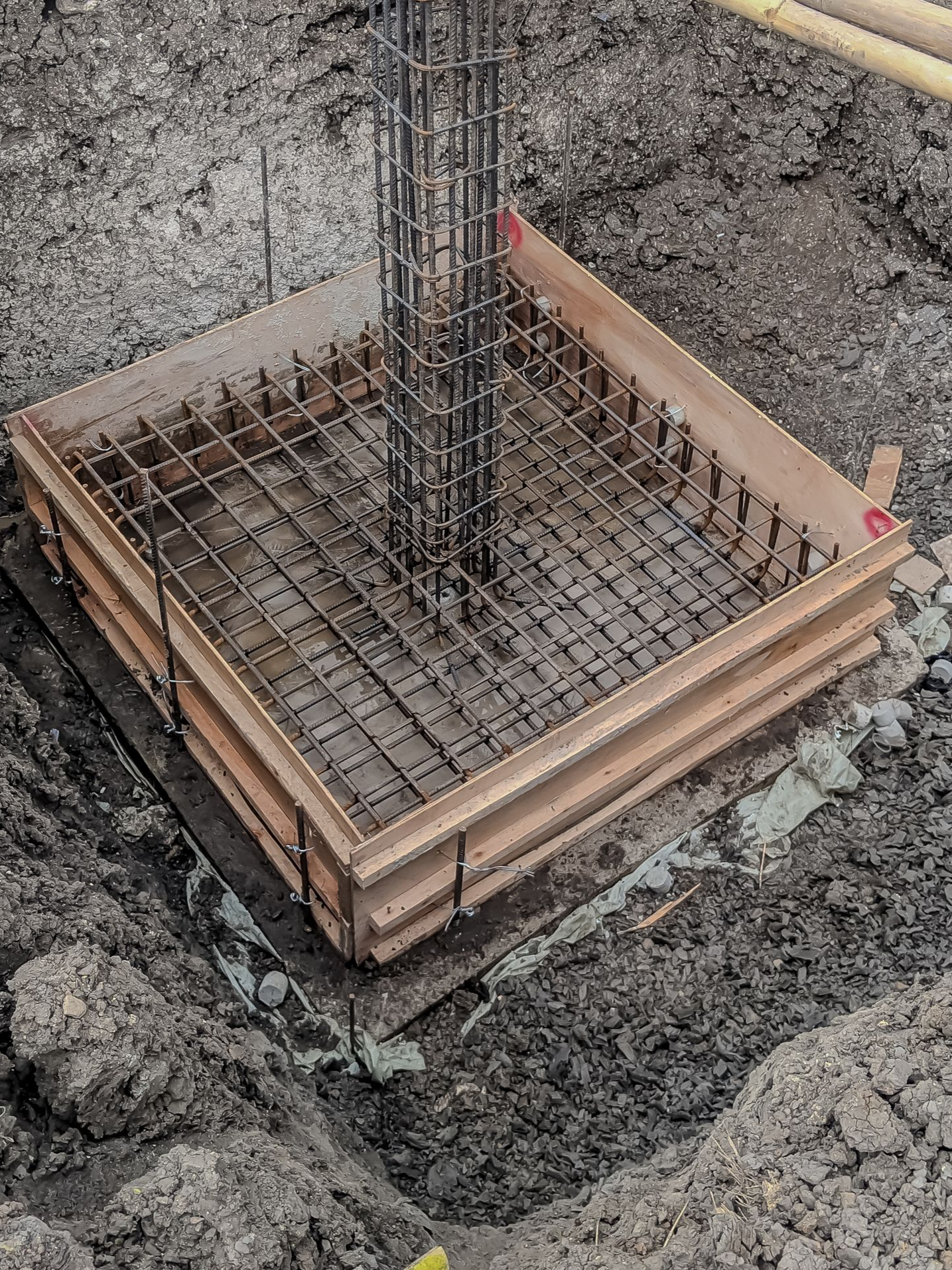 Coffrage carré en bois, fer à béton et colonne centrale dans une fosse en terre.