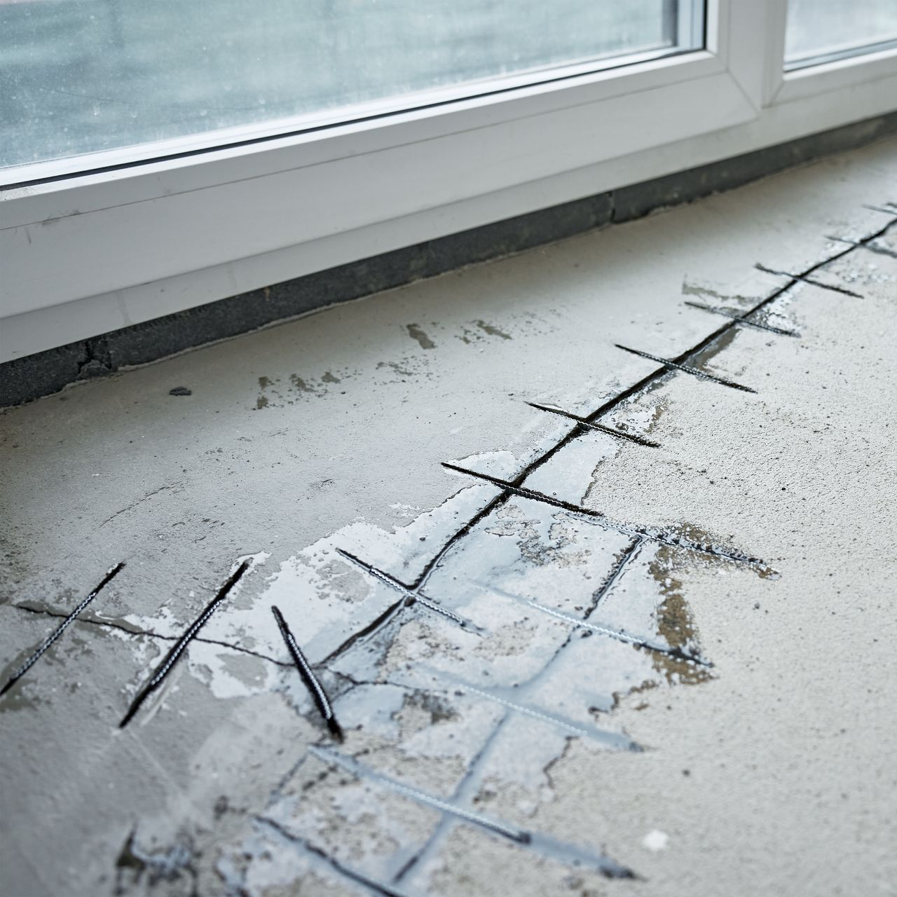 Sol en béton avec des découpes en forme de grille pour les réparations, près d'une fenêtre.
