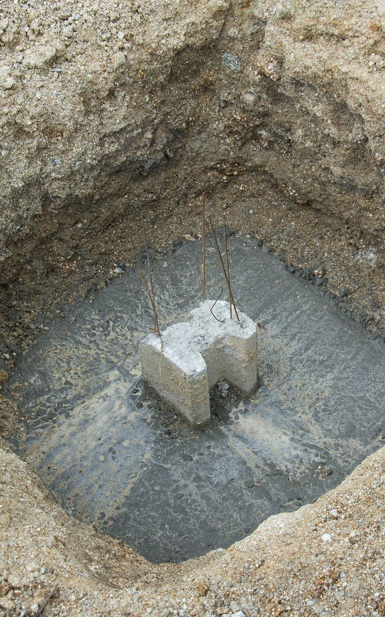 Fondations en béton dans un trou carré, avec barres d'armature en saillie.