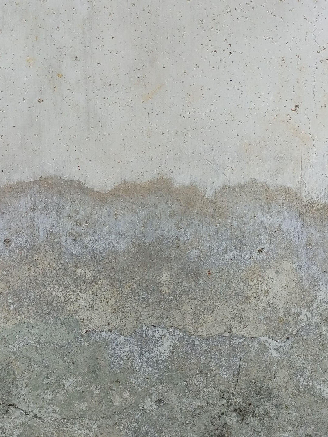 Mur blanc cassé avec dégâts d'eau et décoloration près du bas, affichant différentes nuances de gris.