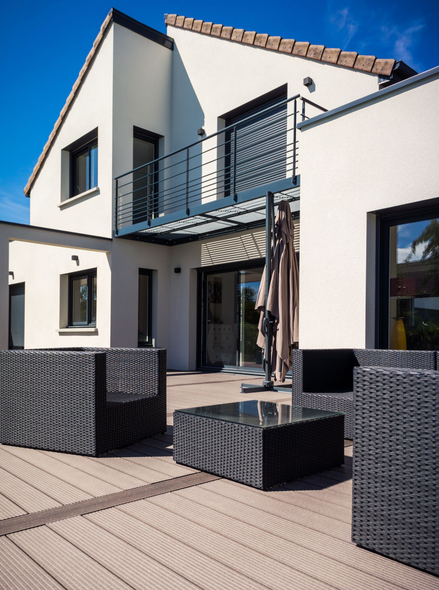 Maison moderne avec patio, meubles en osier et balcon.