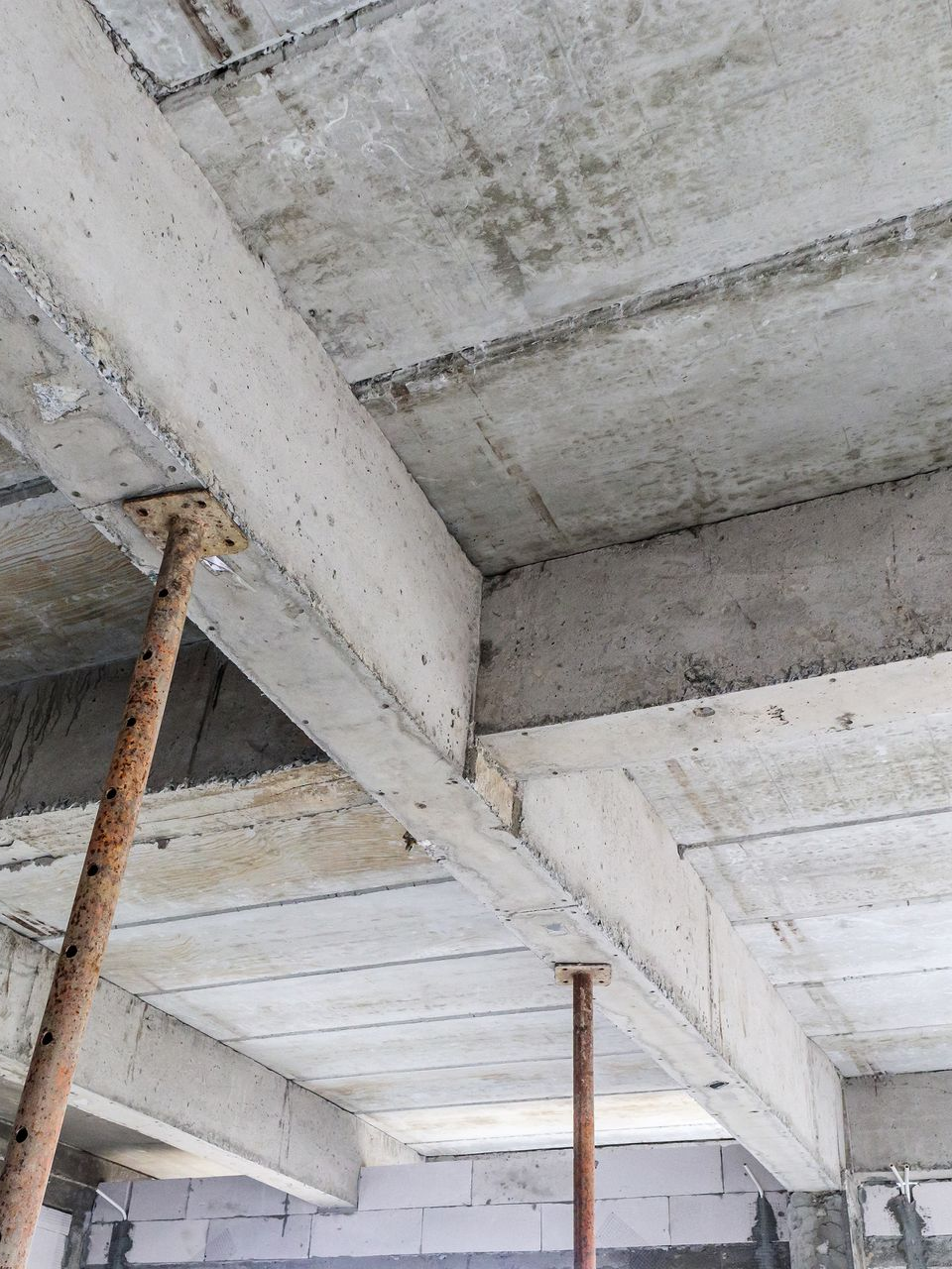 Plafond en béton et poutres soutenues par des poteaux métalliques dans un bâtiment en construction.