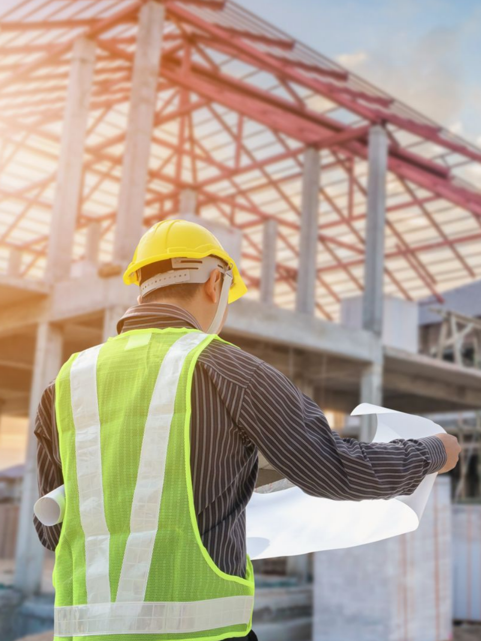 Un ouvrier du bâtiment portant un casque et un gilet jaunes examine des plans sur un chantier de construction.