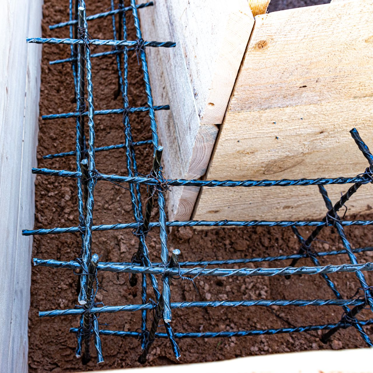 Barres d'acier renforcées formant un coin dans un coffrage en bois rempli de terre pour construction en béton.