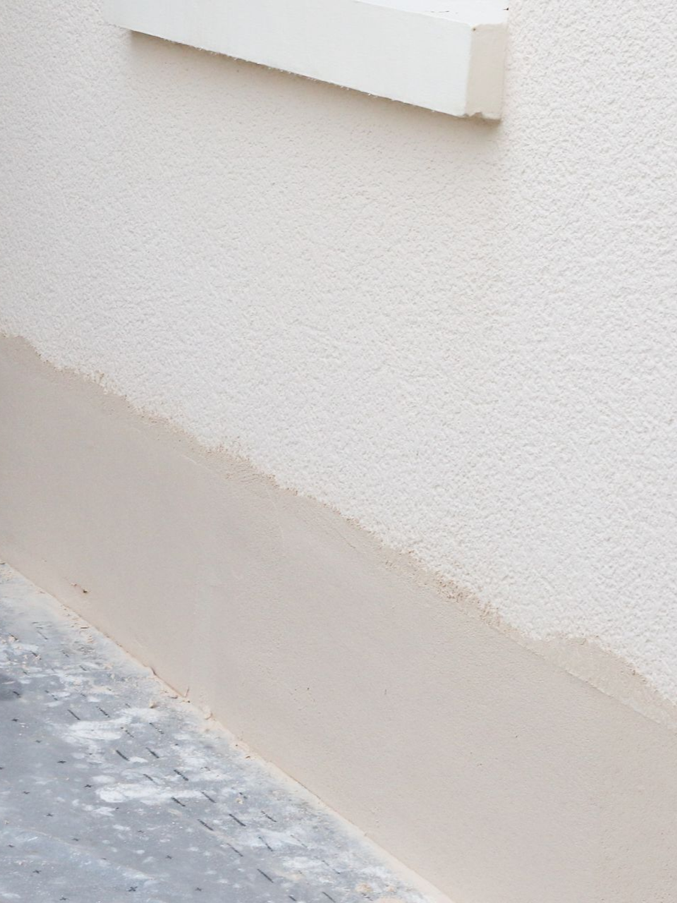 Mur texturé blanc avec une partie inférieure peinte en beige clair rencontrant un sol gris.