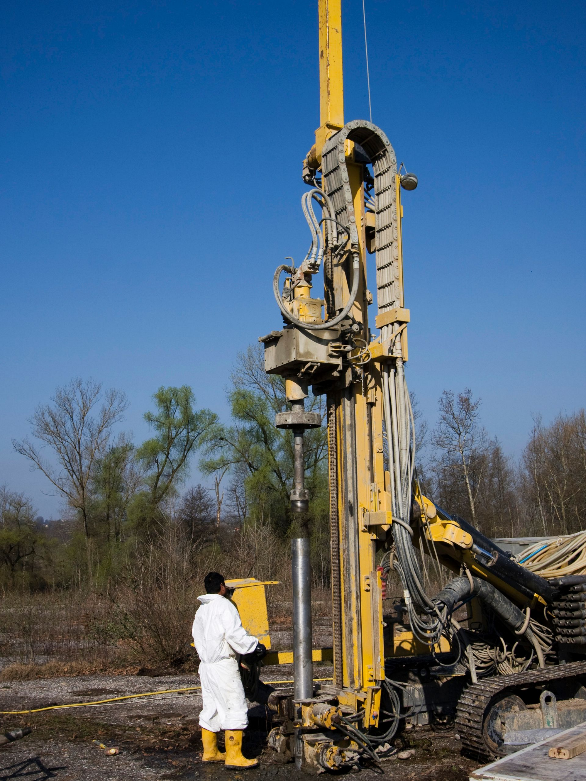 Plate-forme de forage jaune avec un ouvrier en costume blanc et bottes, à l'extérieur.