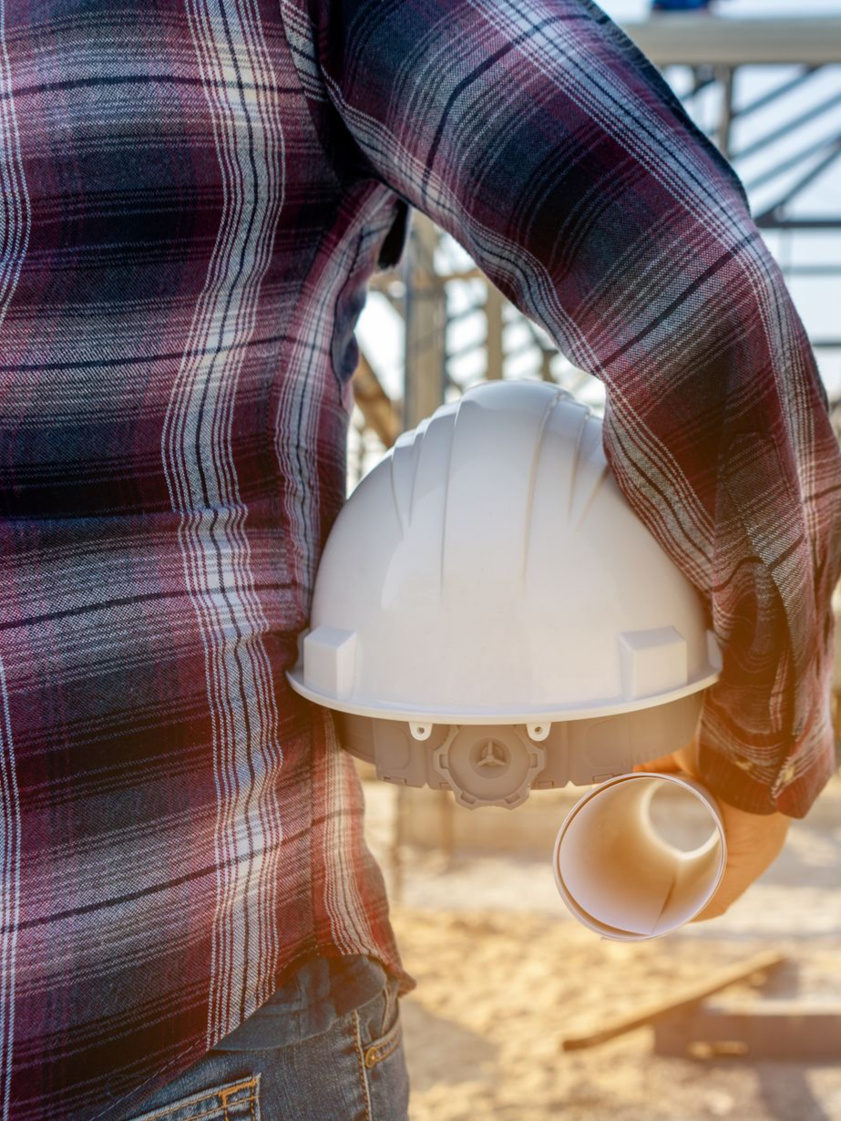 Ouvrier du bâtiment tenant un casque blanc et des plans roulés à l'extérieur.