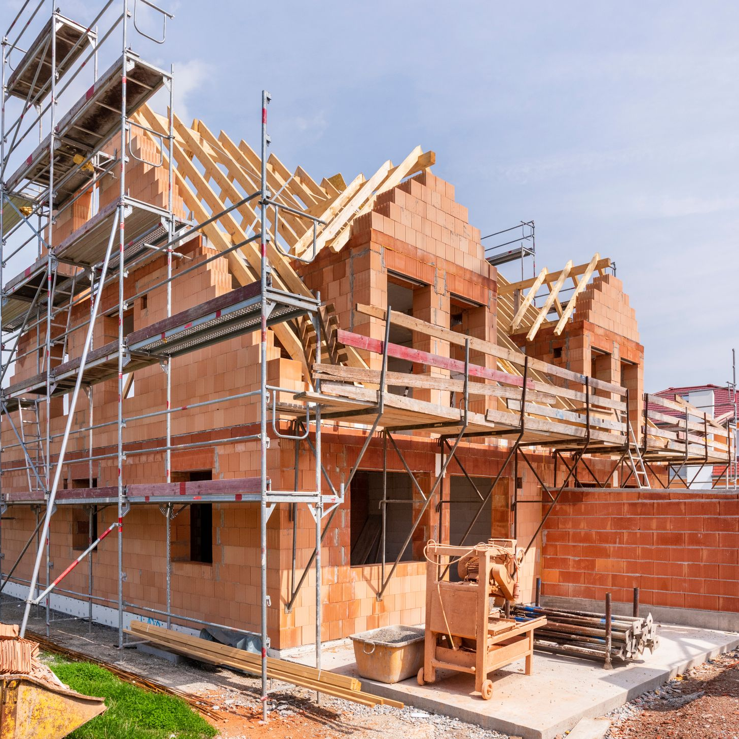 Maison en construction, briques rouges, charpente en bois, échafaudage, extérieur.