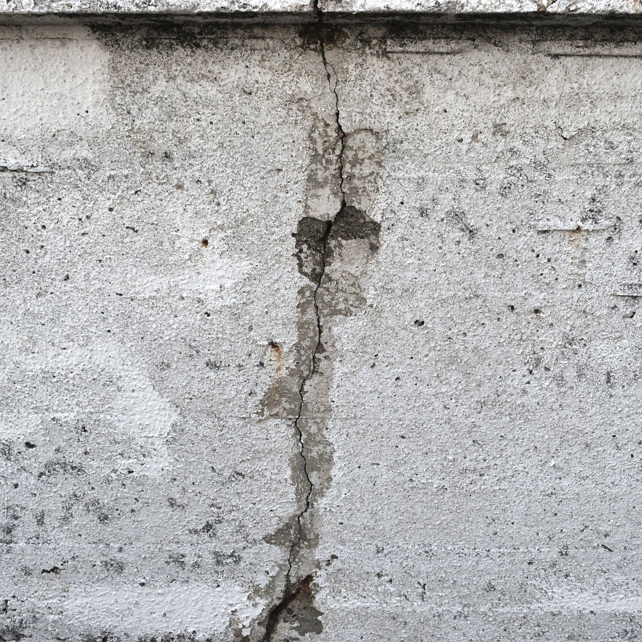 Gros plan d'un mur en béton patiné présentant une fissure verticale proéminente.