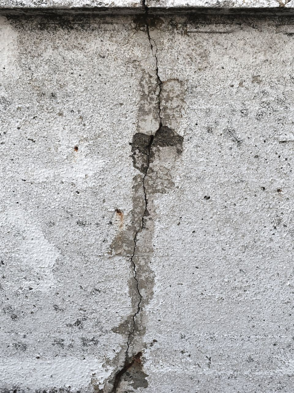 Gros plan d'un mur en béton gris et patiné avec une fissure verticale.