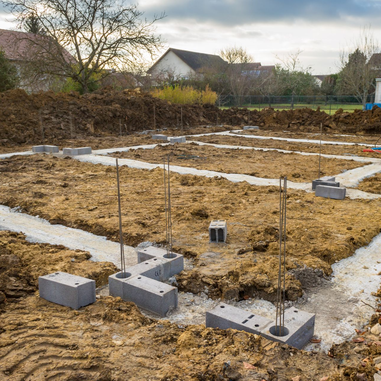 Chantier de construction avec blocs de fondations et barres d'armature, prêt pour la construction d'une structure dans un quartier résidentiel.