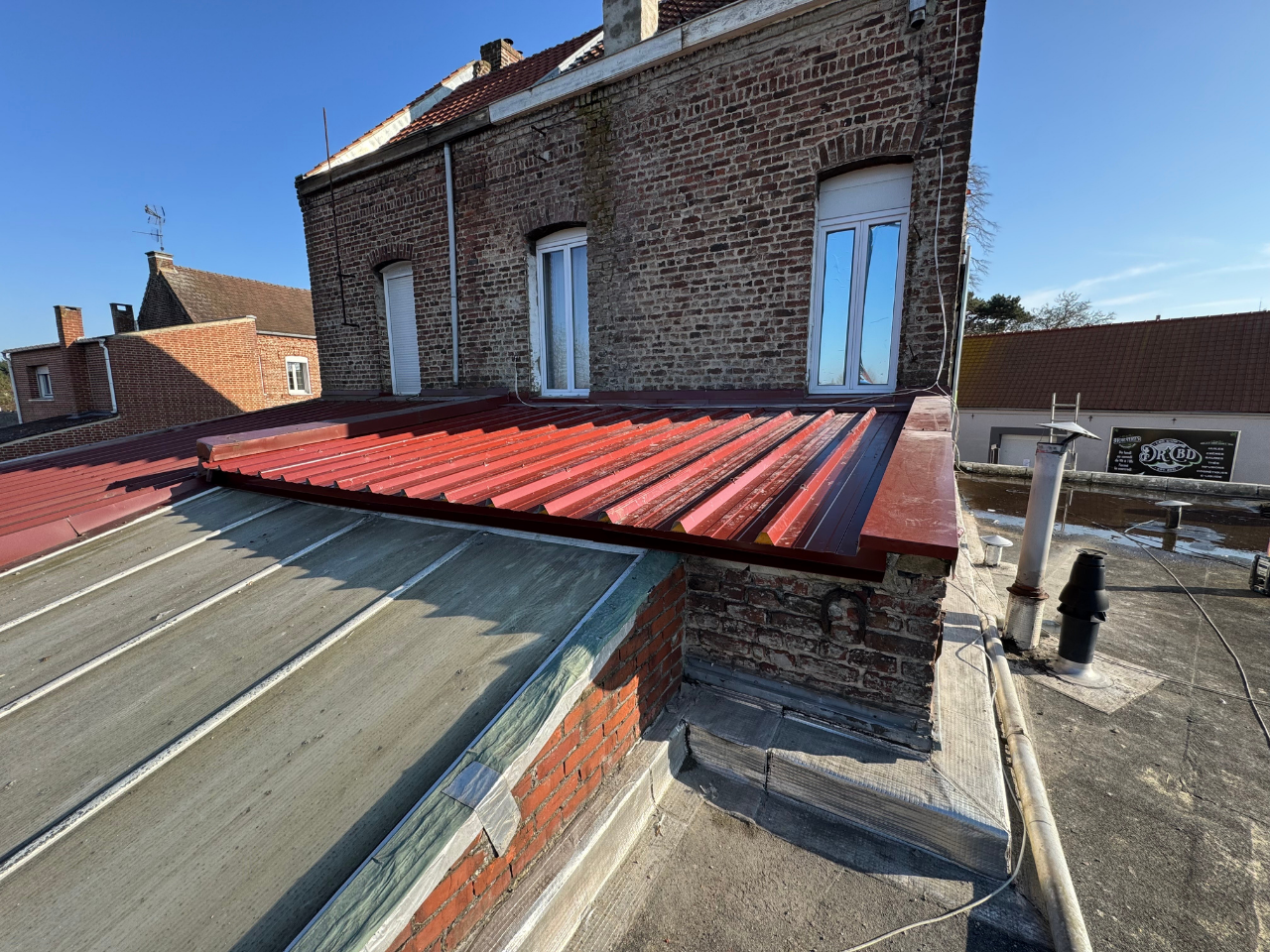 Toit en tôle ondulée rouge sur un bâtiment en briques, journée ensoleillée.