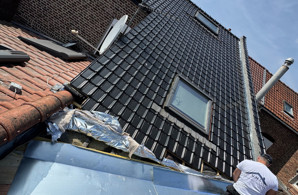 Un toit avec des tuiles sombres, une lucarne et une personne qui travaille dessus ; des bâtiments en briques l'entourent.