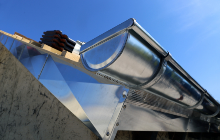 Gouttière en métal brillant installée sur un toit sous un ciel bleu vif.