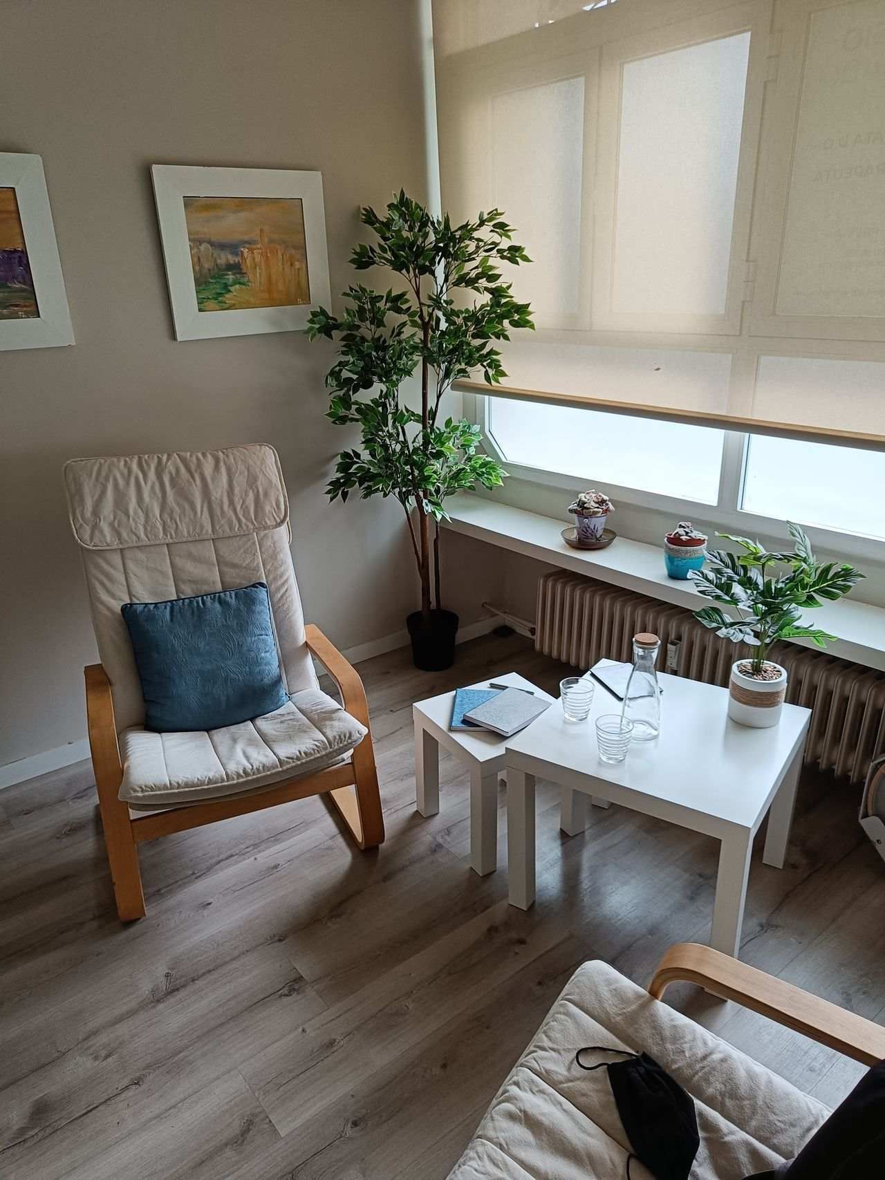 Acogedora sala de estar con sillas de mimbre, mesa de centro blanca, plantas y luz natural tenue.