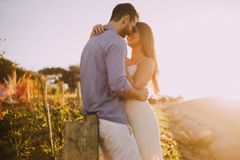 Una pareja se abraza en un campo soleado al atardecer, con una cálida luz dorada y hierba alta.