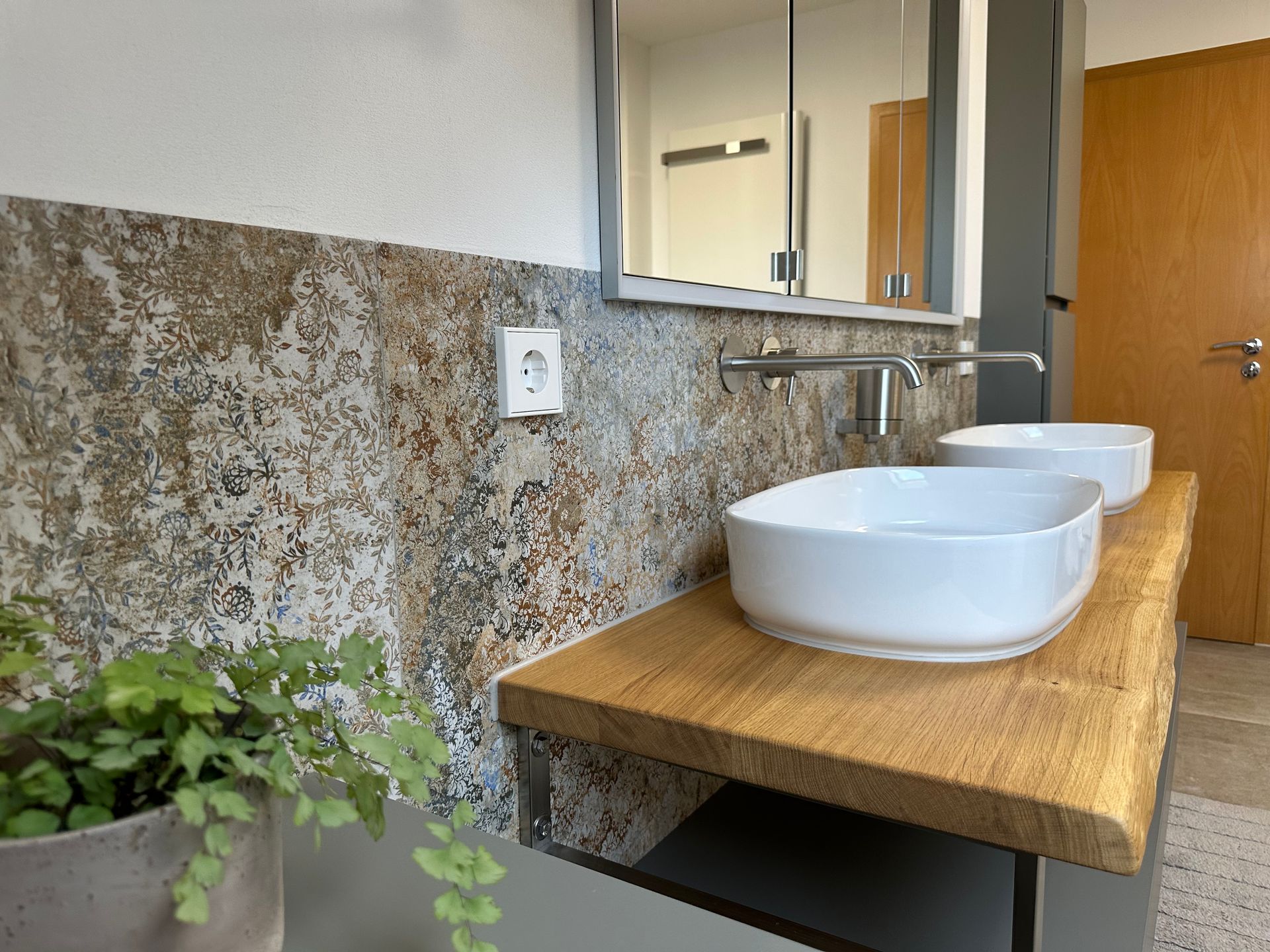 Modernes Badezimmer mit Waschtisch aus Holz, zwei weißen Aufsatzwaschbecken, Spiegel und einer Pflanze