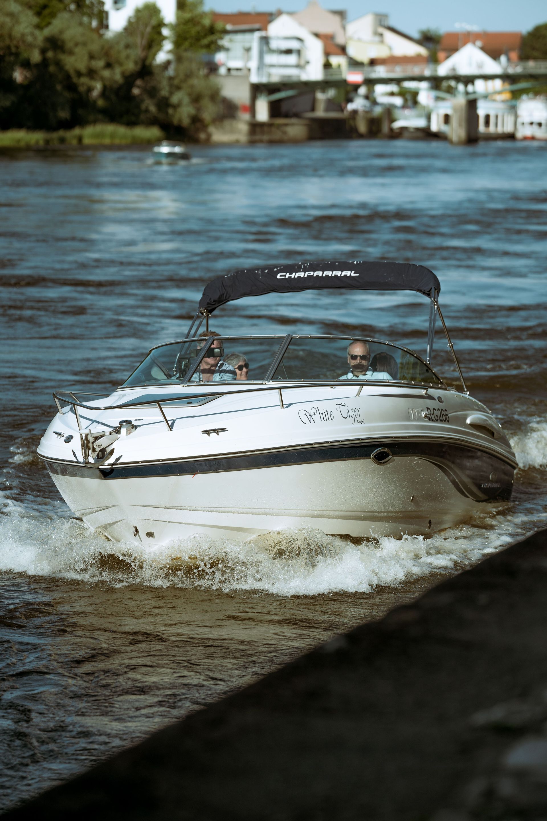 Un hors-bord blanc fend les eaux agitées près d'une rive bordée de maisons.