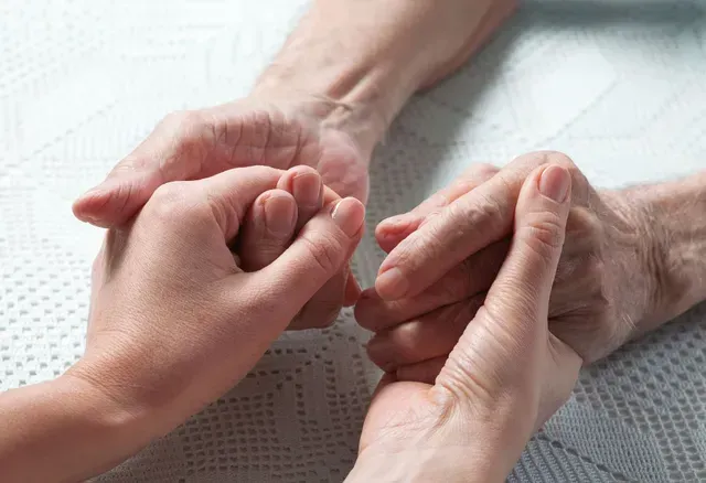 Manos que se toman suavemente una de la otra sobre una superficie cubierta de encaje blanco.