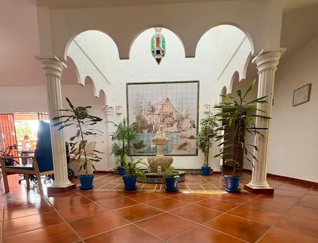 Patio con suelo de terracota, arcos blancos, plantas en macetas y un mural en la pared del fondo.