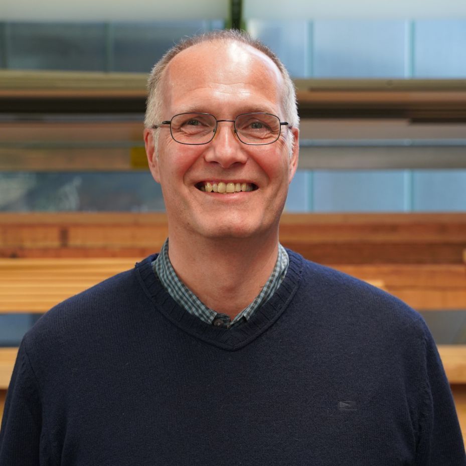 Ein Mann mit Brille und blauem Pullover lächelt in die Kamera