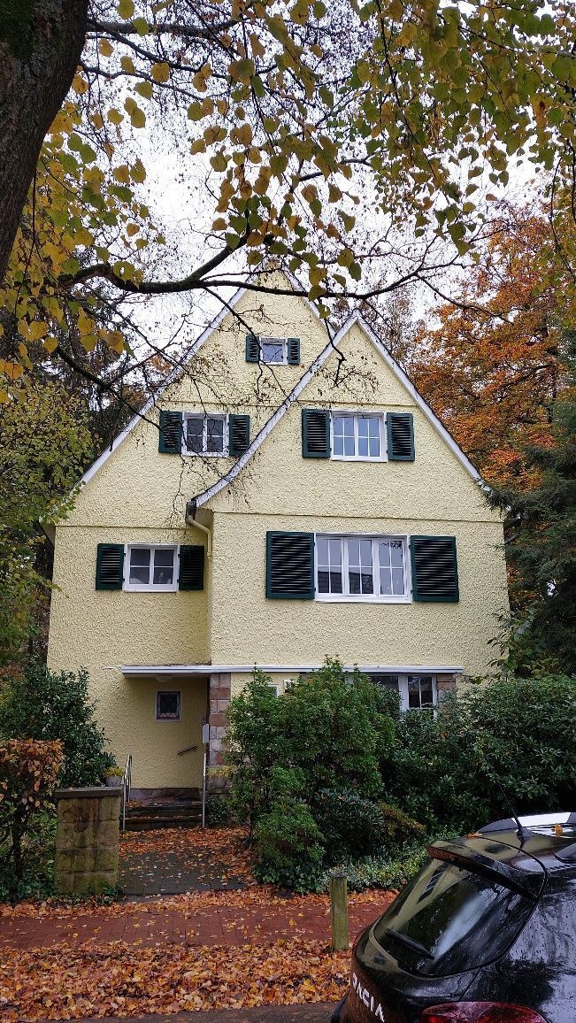 Ein gelbes Haus mit schwarzen Fensterläden und einem davor geparkten Auto.