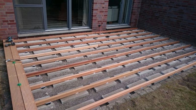 Vor einem Backsteingebäude wird eine Holzterrasse errichtet.