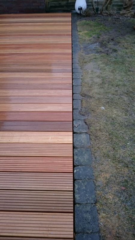 In einem Hof befindet sich neben einem Ziegelweg ein Holzdeck.