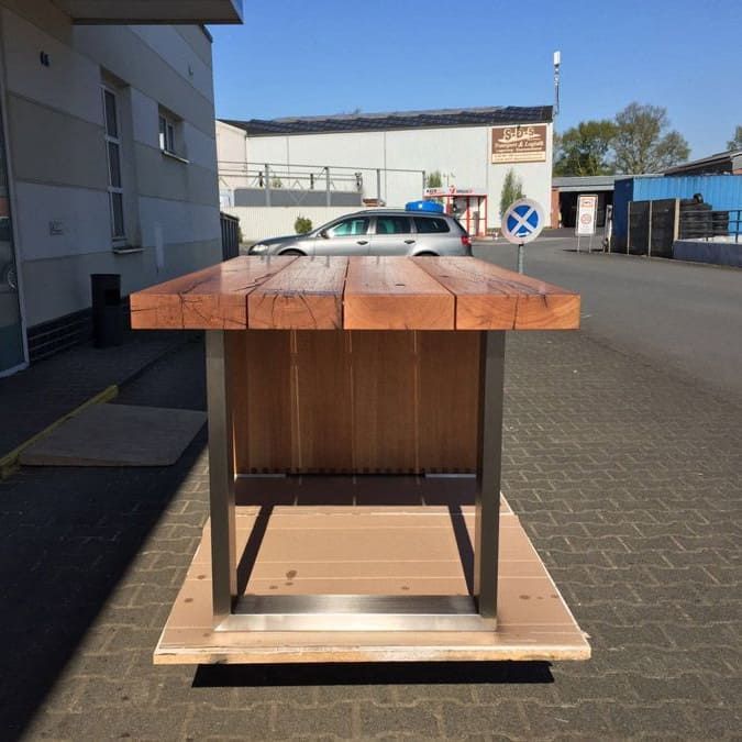 Ein Holztisch steht auf einem gemauerten Gehweg vor einem Gebäude