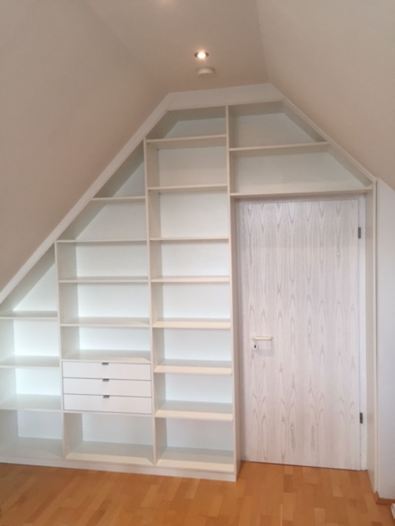 Ein Raum mit schräger Decke und vielen Regalen und Schubladen