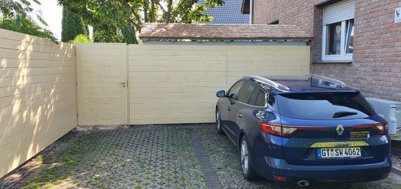 Ein blaues Auto steht in einer Einfahrt neben einem Zaun.