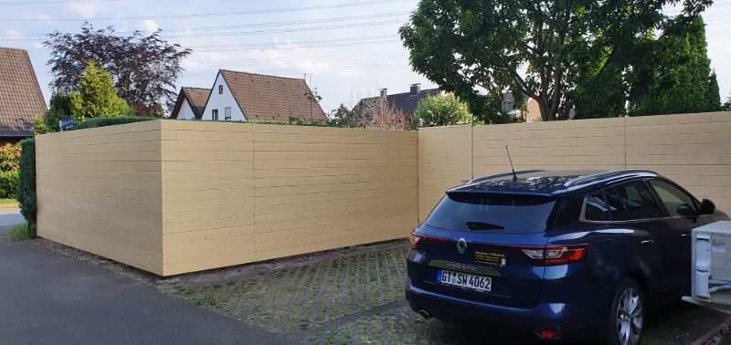 Vor einem Holzzaun parkt ein blaues Auto.