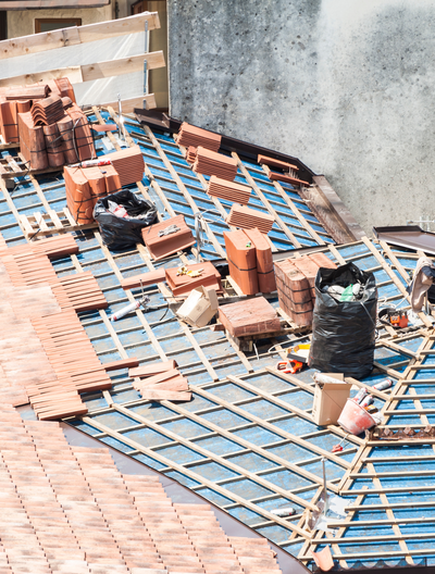 Toiture en construction avec des briques rouges, des débris et des bâches en plastique.