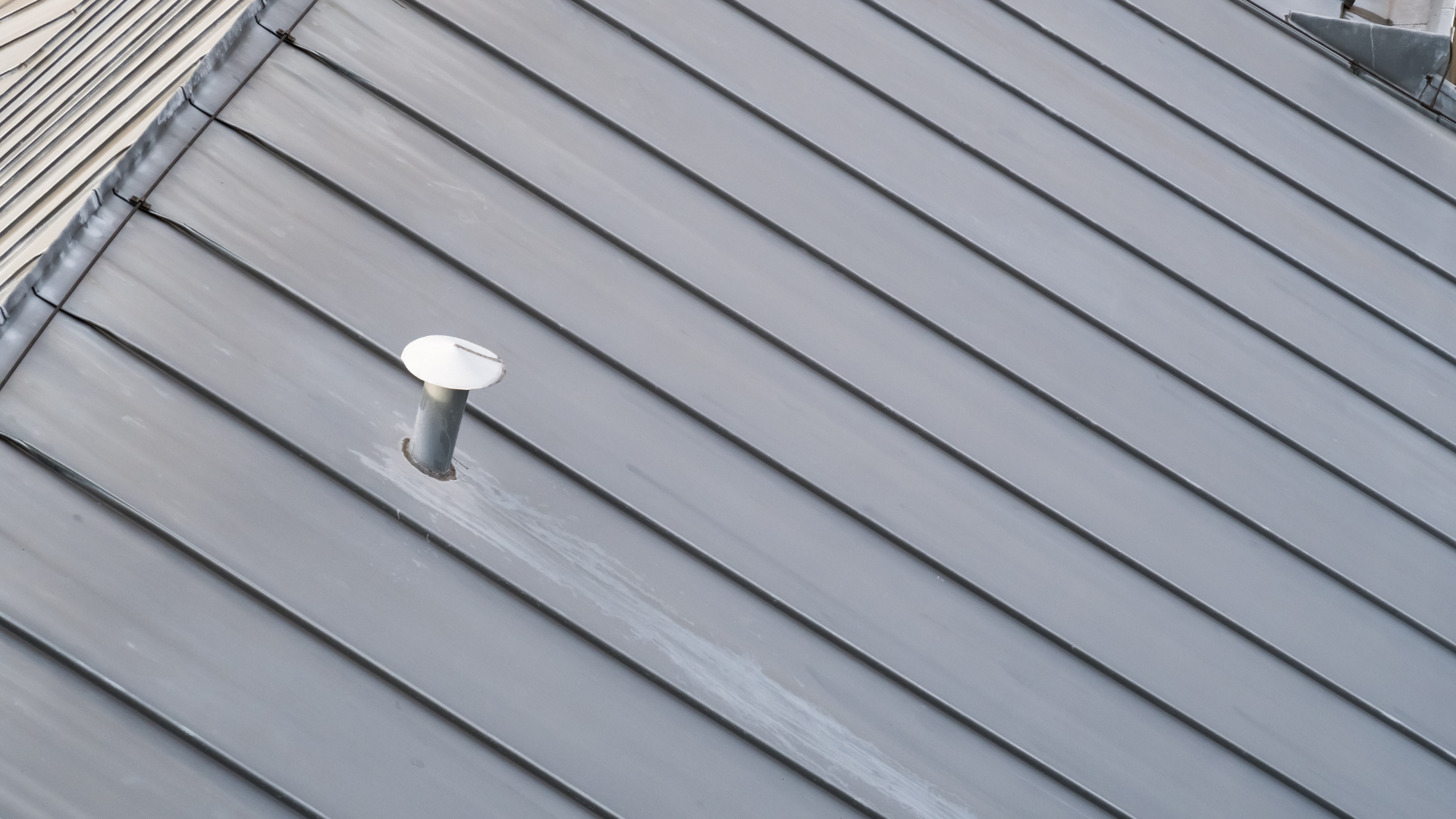 Toiture métallique grise avec un petit tuyau d'aération et un chapeau blanc.
