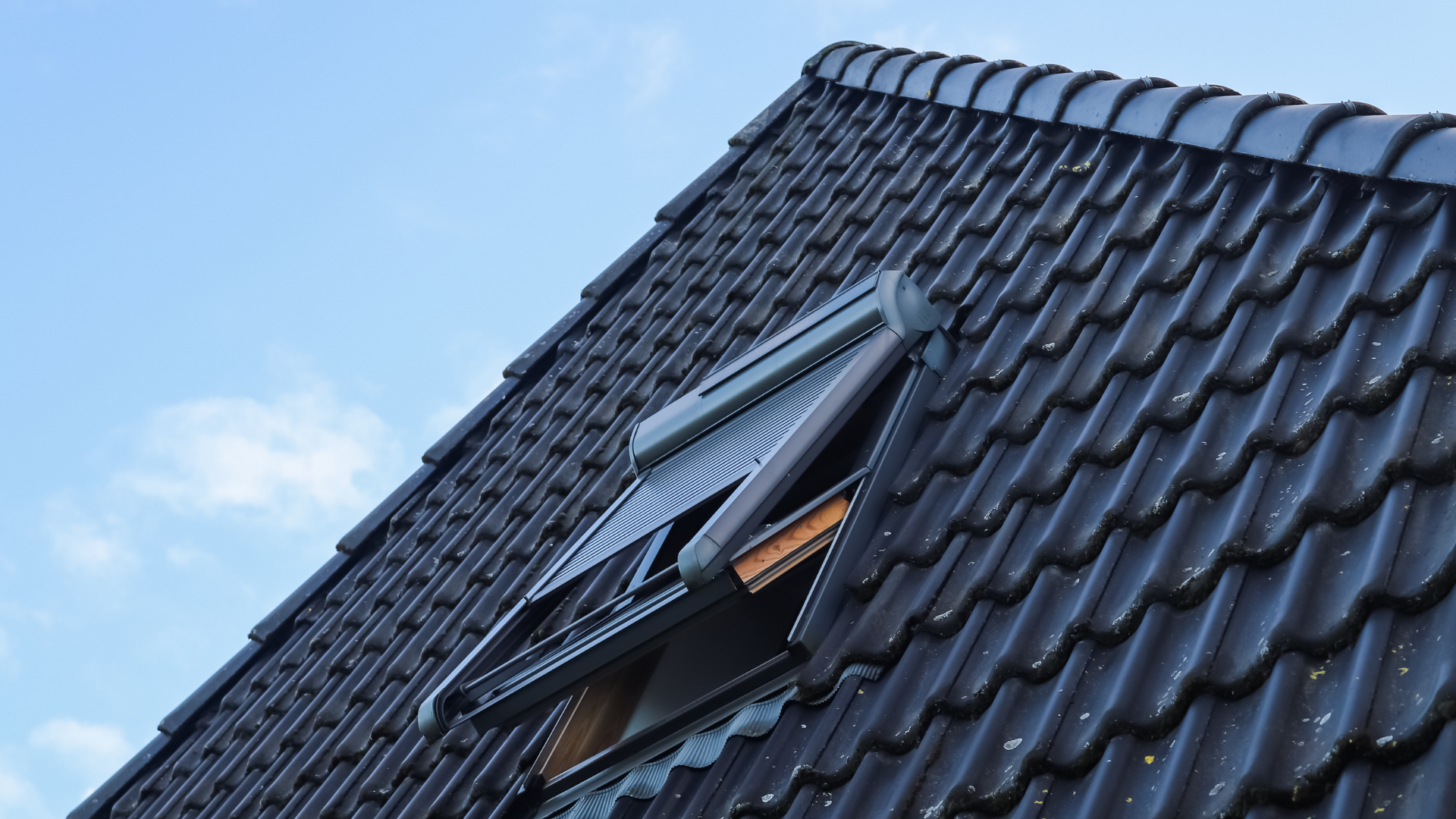 Toit de tuiles noires avec puits de lumière ouvert sur un ciel bleu.