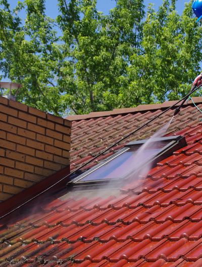 Une personne nettoie au nettoyeur haute pression un toit de tuiles rouges.
