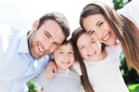 Familia de cuatro sonriendo y abrazándose al aire libre.