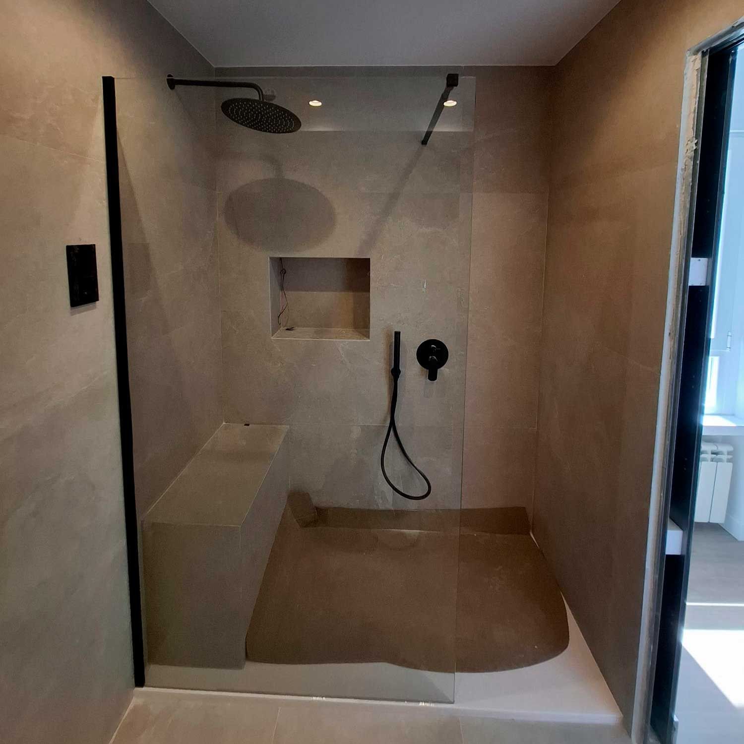 Un baño con ducha a ras de suelo con puerta de cristal y cabezal de ducha.