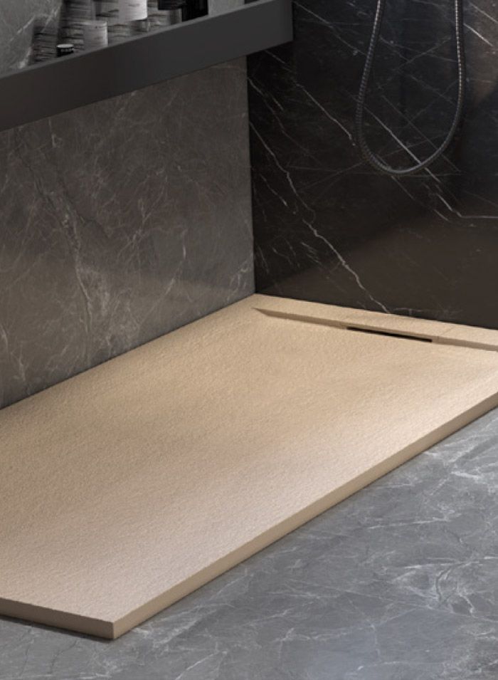 Base de ducha rectangular de color tostado con una ranura de drenaje estrecha, colocada sobre paredes de azulejos oscuros y veteados.