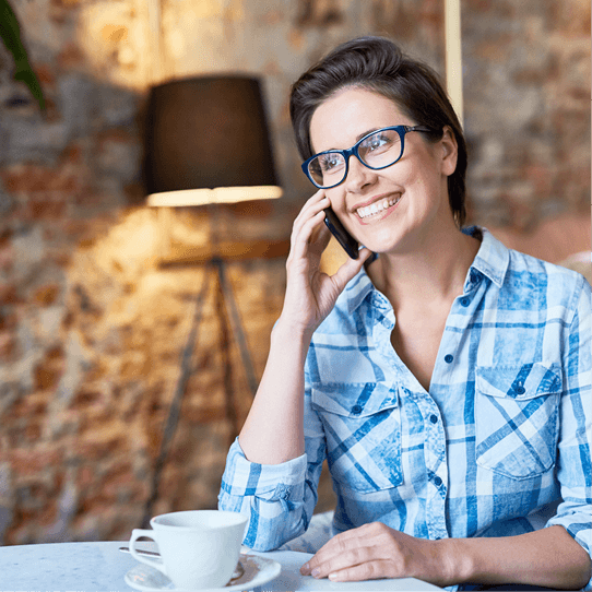 Eine Frau mit Brille sitzt an einem Tisch und telefoniert mit einem Mobiltelefon.